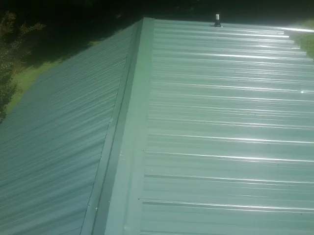 New green metal panels meeting at the ridge of a roof — Flat Roof Repair work by our crew in Wheatland