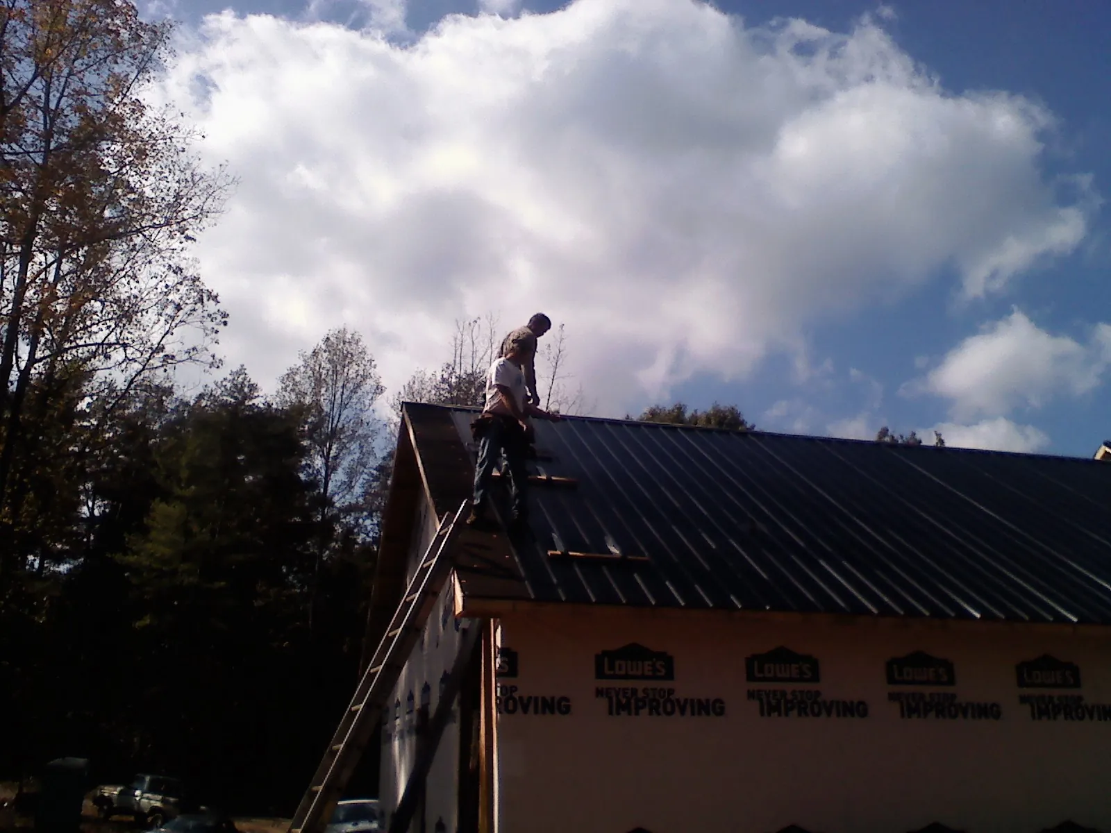 Roofer fastening dark metal panels high against a cloudy sky, from a Roof Inspection job in Wheatland